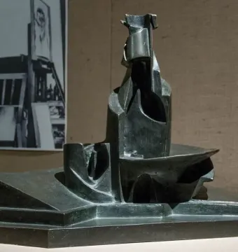 Dark abstract sculpture of Development of a Bottle in Space on a light surface, with a black-and-white studio photograph in the background.