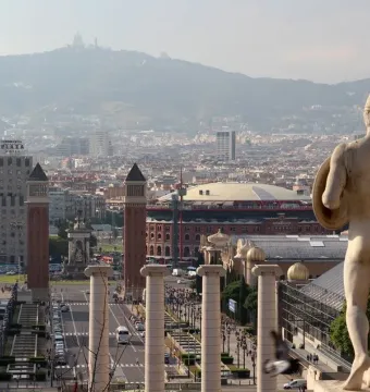 The Four Columns standing on Montjuic with a city street and buildings below.