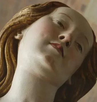Close-up of Mary Magdalene’s sculpted face with wavy golden hair and red lips.