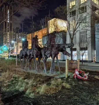 The Partisans sculpture in Boston, shown at night with figures on horseback, a memorial plaque, and a floral wreath at the base.