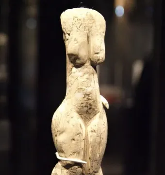 Venus of Eliseevichi carved figurine with prominent breasts and hips, shown on a support against a dark background.