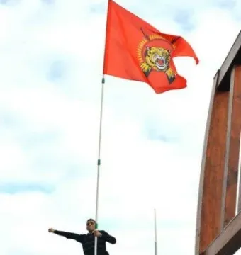 Broken Chair sculpture with a man standing on it and holding a red flag against a cloudy sky.