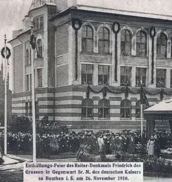 Equestrian Monument of Frederick the Great on a tall pedestal, with a crowd gathered around it and flagpoles nearby.