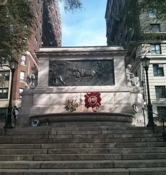 Firemen\'s Memorial stone monument with a bas-relief panel, wreaths at the base, and ornate lampposts along Riverside Drive.