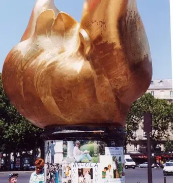 Flame of Liberty monument with photos and messages at its base, with an adult and child nearby.