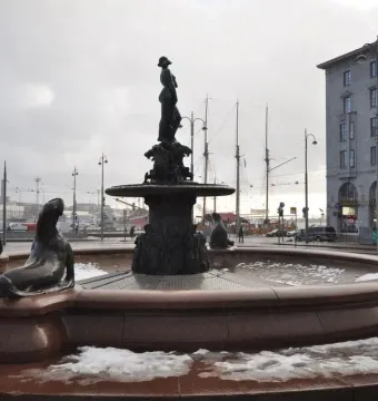 Havis Amanda fountain with a bronze female statue on a pedestal, surrounded by sea lion figures and patches of snow.