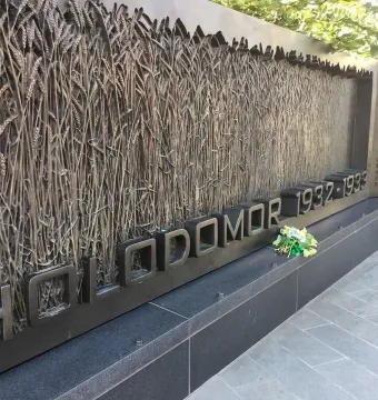 Holodomor Memorial wall with wheat stalk relief and flowers placed below the HOLODOMOR 1932-1933 inscription.