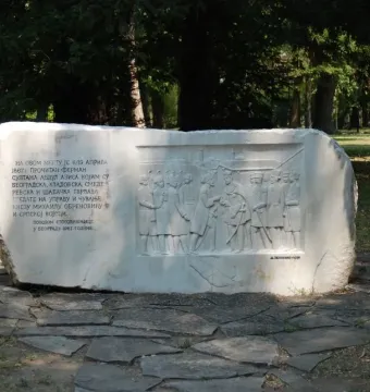 Keys Handover Memorial with a stone relief of several figures and Cyrillic inscription in a park