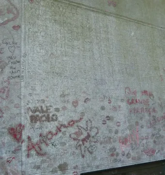 Oscar Wilde\'s tomb covered with graffiti, handwritten messages, hearts, and red lipstick kiss marks.