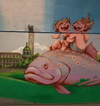 Mural inspired by the Rhine Water Fountain showing two cherubic figures riding a spotted pink fish over green hills with a city skyline behind them.