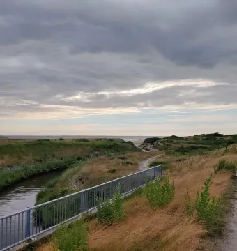 The Man by the Sea sculpture appears in the far right distance against a cloudy coastal landscape.