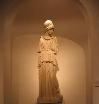 Draped statue of Athena wearing a helmet, standing on a dark pedestal in a recessed arched alcove.