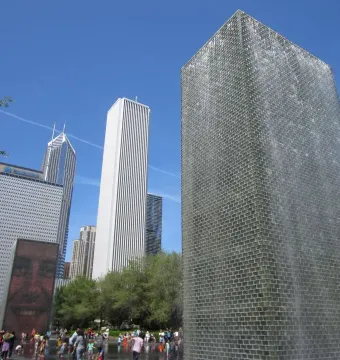 Crown Fountain with water cascading down one tower and a projected face on the other, with people gathered in the shallow pool below.