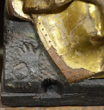 Close-up of a burnt hand imprint on the Fisenne Altarpiece, showing dark carved wood and worn gold leaf.
