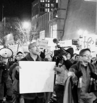 A white LOVE sign with a tilted O held above a crowd at a nighttime protest.