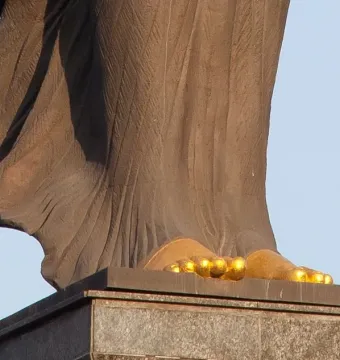 Lower part of the Statue of Sofia showing bare feet and draped stone folds on a dark pedestal.