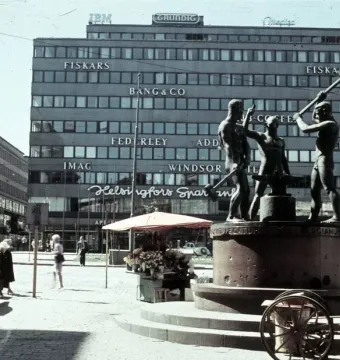 The Three Smiths bronze monument showing three men hammering an anvil on a stone base in a city square.