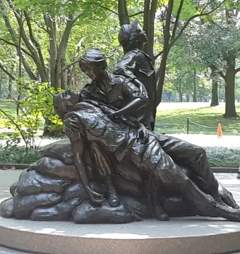 Vietnam Women\'s Memorial bronze sculpture showing three figures on a circular base in a leafy park setting.