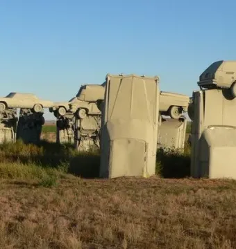 Carhenge sculpture made of tan-colored cars standing in a dry grassy field under a clear blue sky.