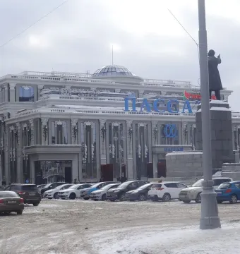 Lenin Monument on a snowy stone pedestal beside a light pole, with an ornate building in the background.