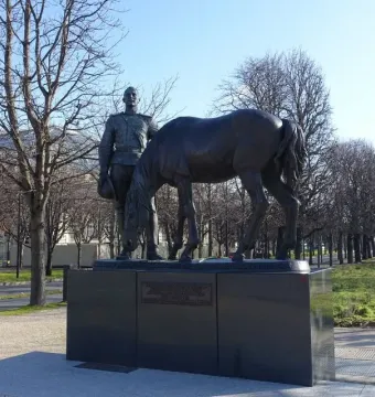 Monument to the Russian Expeditionary Force, showing a dark metal military figure beside a grazing horse on a stone base in a park.
