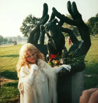 Person standing beside the Monument to Dog Jock, a dark sculpture of a dog held by stylized hands, decorated with a red ribbon and greenery.