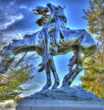 End of the Trail bronze sculpture of a weary rider slumped over a bowed horse against a blue sky.