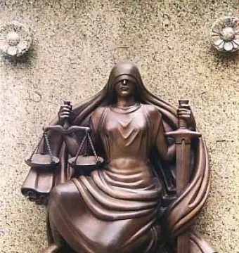 Bronze relief sculpture of Lady Justice holding scales and a sword against a stone wall.