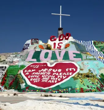 Salvation Mountain with a white cross on top, covered in colorful painted religious messages and symbols.