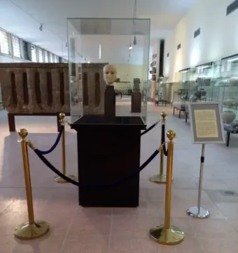 The Warka Mask displayed in a glass case on a dark pedestal in a museum hall.