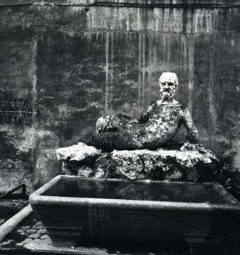 Babuino Fountain with a weathered reclining bearded stone statue above a small basin.