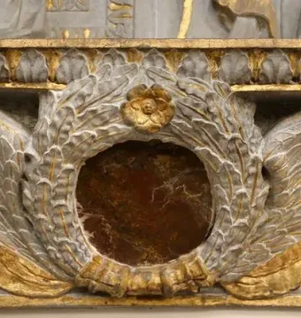 Close-up of the Cavalcanti Annunciation showing a reddish-brown circular medallion framed by sculpted wings, a leafy wreath, and a ribbon.