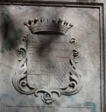 Weathered stone coat of arms relief with a crown, ornate scrolls, and the inscription TENENTE GENERAL.