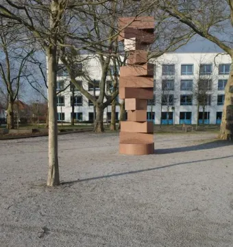 Endlose Treppe sculpture by Max Bill in an open gravel courtyard, with a plaque in the foreground and a modern white building behind it.