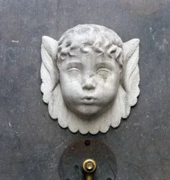 Font de Santa Eulàlia: a weathered stone cherub head above a brass water spigot on a dark wall.