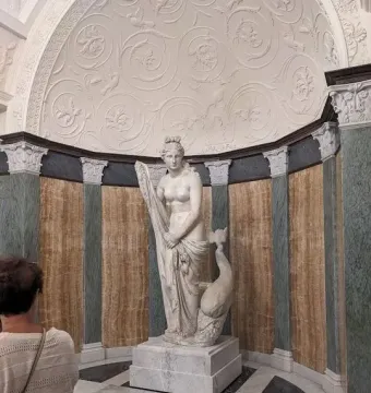 Mazarin Venus statue on a stone pedestal in an alcove, with a visitor standing nearby.