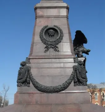 Lower section of the Monument of Alexander III with a bronze bust relief, draped garland, and a winged eagle on a granite pedestal.