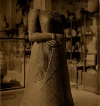 Headless stone statue of Napir-Asu with hands clasped across the midsection and a pleated long garment.
