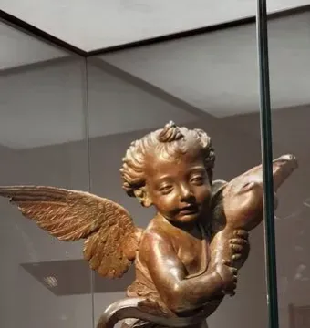 Bronze Putto with a Dolphin sculpture displayed on a white plinth in a glass case.