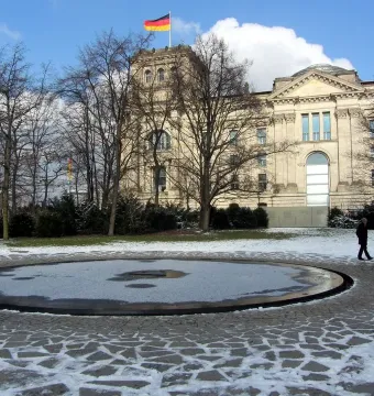 A snow-covered circular basin set in a stone-paved area, with bare trees and a classical-style building in the background.