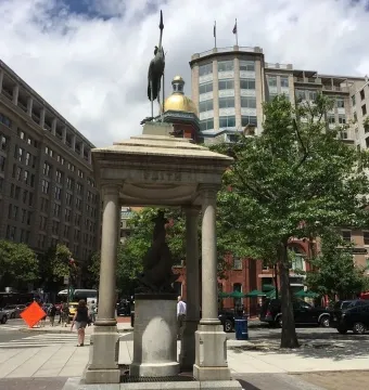 Temperance Fountain, a stone pavilion topped with a crane statue on a busy city sidewalk.
