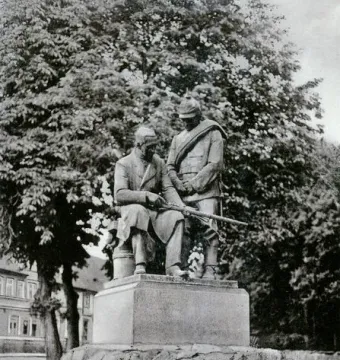 Dreyse Monument with two sculpted male figures on a rocky base, one seated holding a rifle and the other standing behind in uniform.
