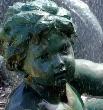 Bronze child statue from the Monument aux Girondins fountain covered in flowing water.