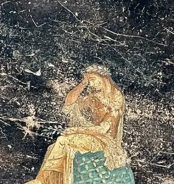 A seated figure in golden robes rests on a patterned blue-green omphalos with a dark background.