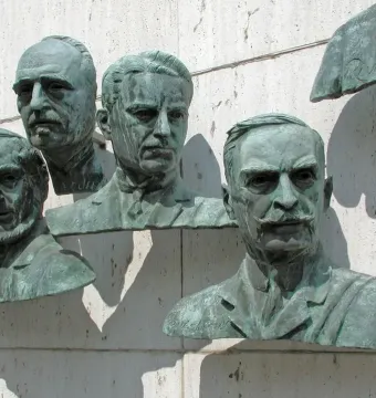 Four bronze busts from the Polio Hall of Fame mounted on a light stone wall, with part of a fifth bust visible.