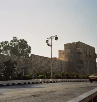 An equestrian statue of Saladin stands beside a massive stone wall with a road curving past it.