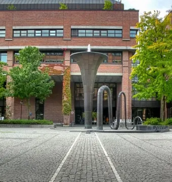Erich-Schulze-Brunnen, a tall trumpet-shaped metal sculpture with water flowing from the top in a cobblestone square.