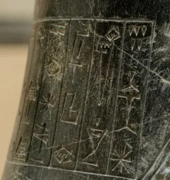 Close-up of the Iddi-Ilum statuette showing deeply incised cuneiform inscriptions on a dark stone surface.