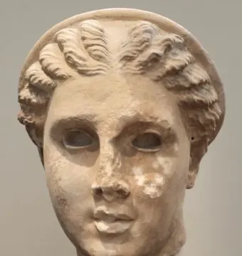 Weathered stone head of Lycosoura Artemis with hollow eyes, wavy hair, and a circular diadem.