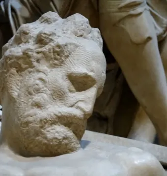 Close-up of Michelangelo’s Dusk showing a marble male figure with a tilted head, textured beard, and shadowed eyes.